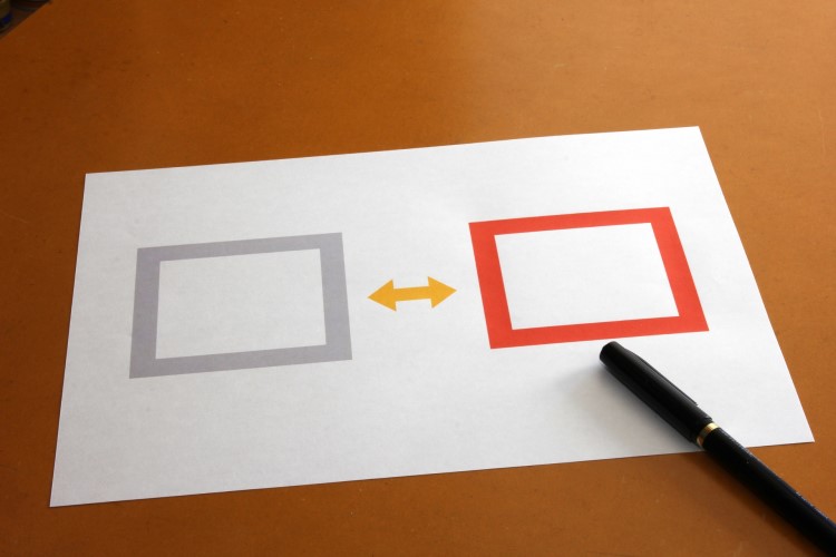 灰色と赤色の正方形と両向き矢印が描かれた紙の上にペン置かれた画像