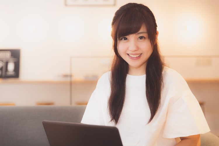 ノートパソコンを前に笑顔で座っている女性の画像