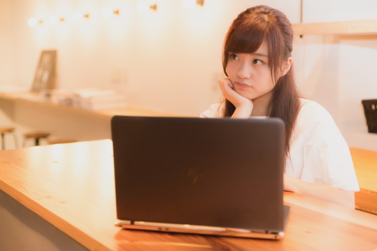 ノートパソコンの前で頬杖をついている女性の画像